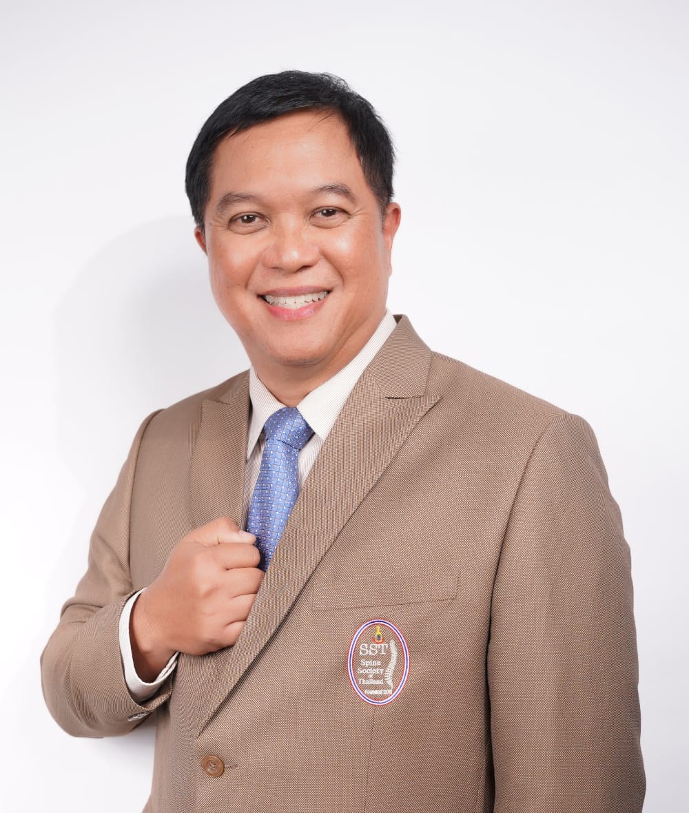กระดูกสันหลัง กรรมการบริหารปัจจุบัน: ชายไทยยิ้มในชุดสูทสีน้ำตาลพร้อมเข็มกลัด SST ออร์โธปิดิกส์