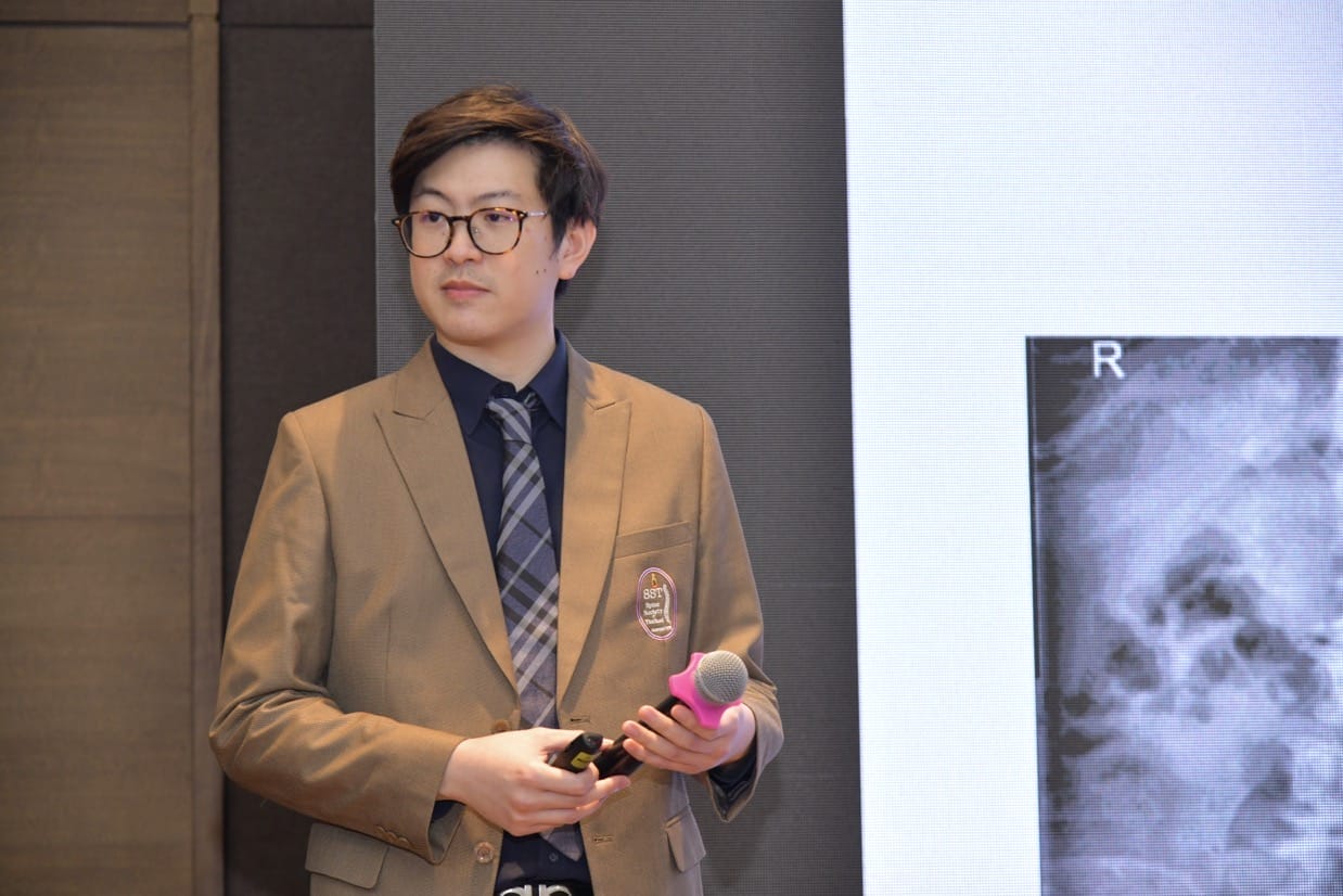 กระดูกสันหลัง ชายใส่สูทสีแทนถือไมโครโฟนข้างภาพเอ็กซ์เรย์ในงานประชุมวิชาการ BASIC SPINE COURSE 2025 ออร์โธปิดิกส์